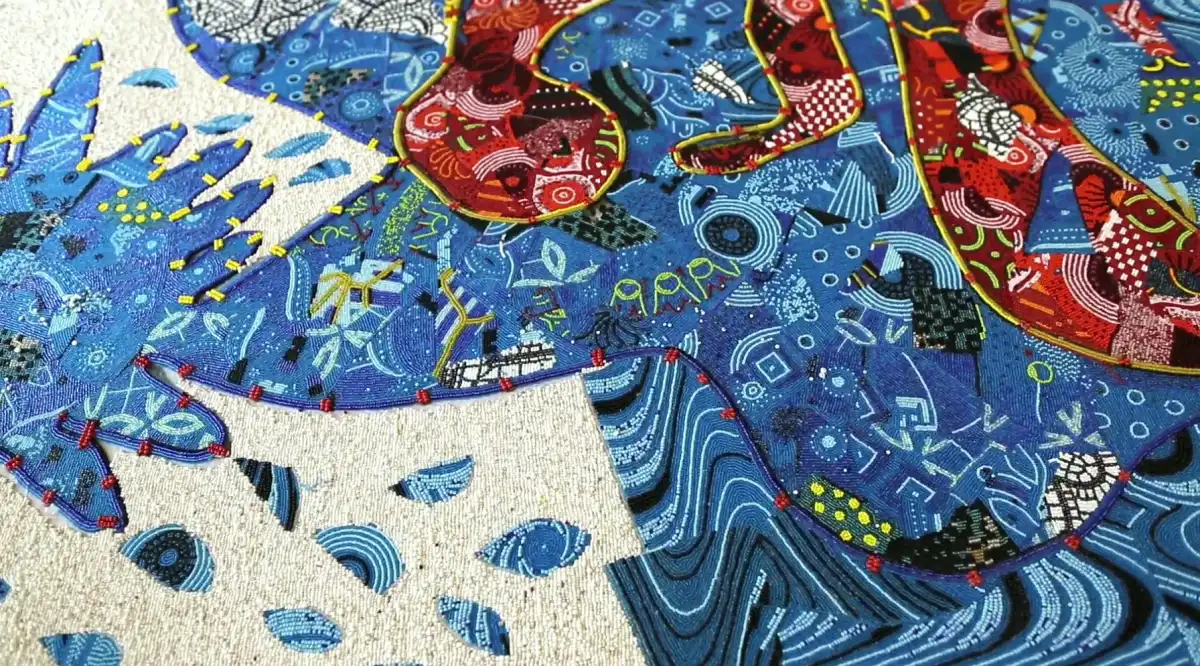 Close-up of a vibrant, abstract textile artwork with swirling blue patterns, red and green accents, and intricate geometric designs.