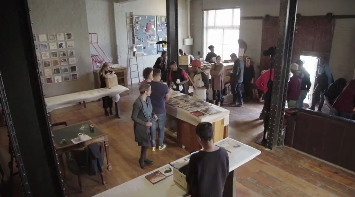 People browsing art and photographs in a spacious, industrial-style gallery with wooden floors and large windows.