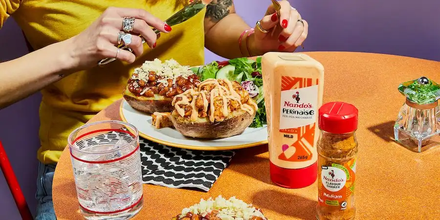 Person enjoying loaded potato skins with Nando's PERinaise and PERi-PERi seasoning on a vibrant table setting.