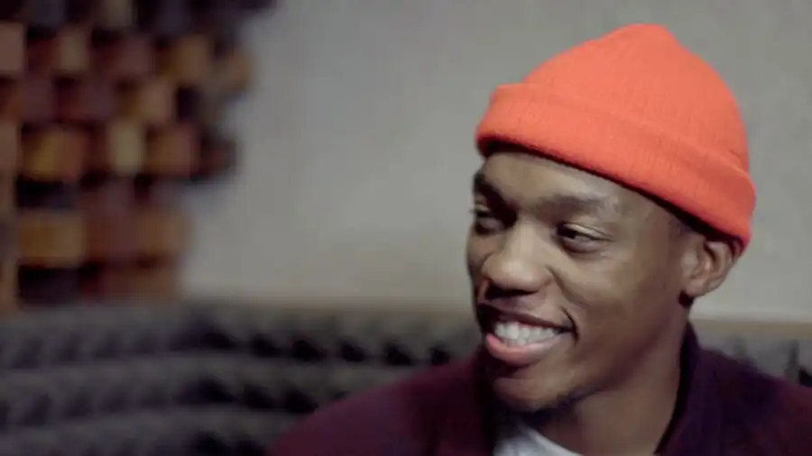 Person wearing an orange beanie, smiling, in a room with acoustic panels.