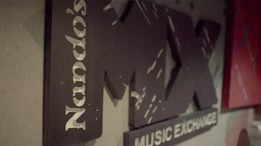 Sign reading "Nando's Music Exchange" on a textured wall, featuring bold lettering and a modern design.