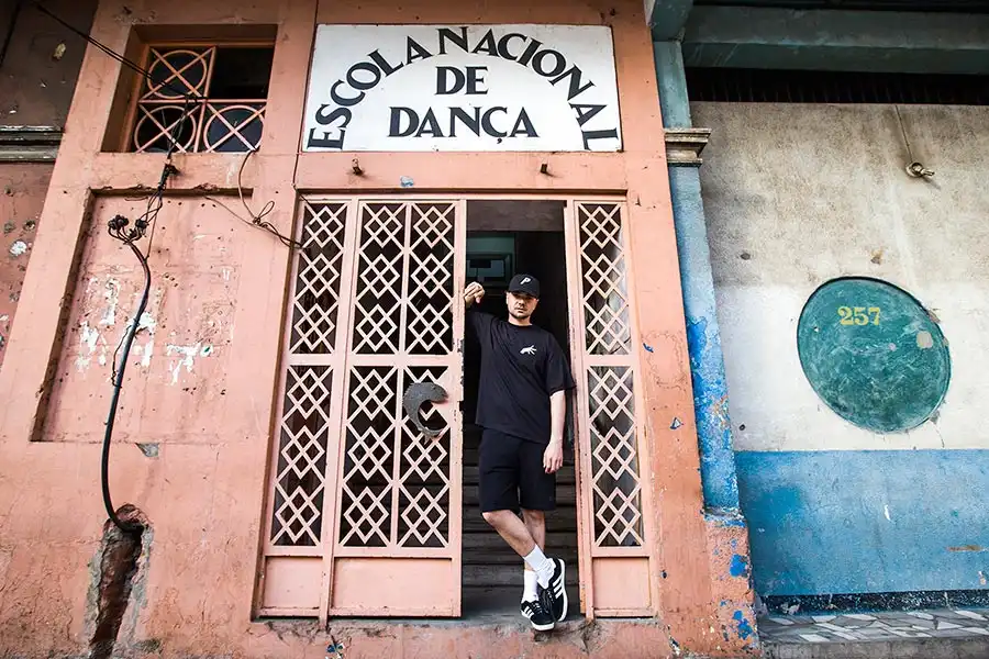 A person leans against the entrance of a weathered building labeled "Escola Nacional de Dança."