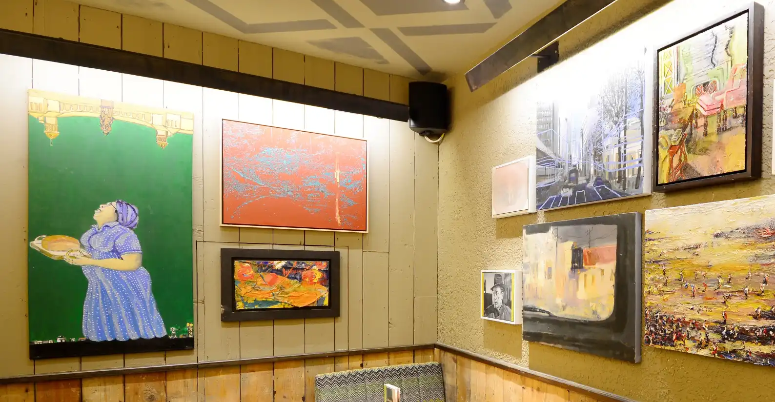 Art-covered wall with diverse paintings in a cozy room, featuring vibrant colors and various styles.