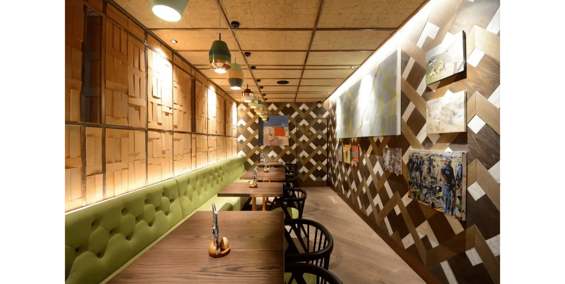 Cozy restaurant interior with wooden decor, green cushioned seating, and modern artwork on the walls. Warm lighting creates an inviting atmosphere.